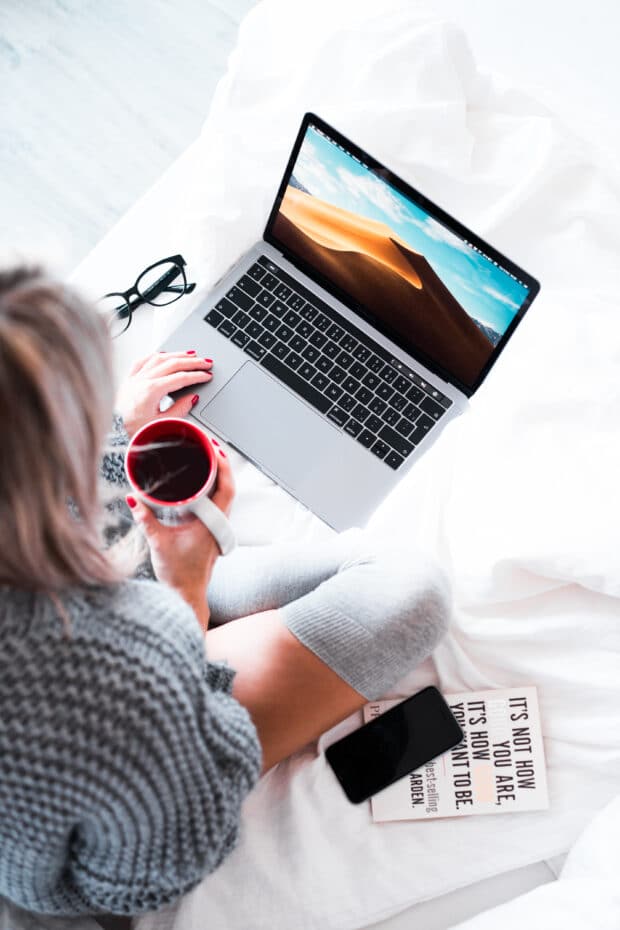 woman holding cup of coffee and working on laptop