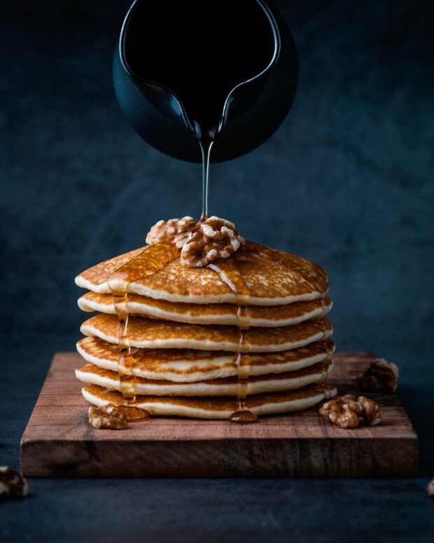 maple syrup pouring onto stack of pancakes with walnuts