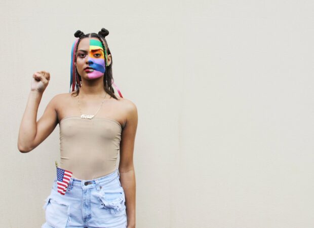 person with face painting of pride flag holding fist for Black Lives Matter movement